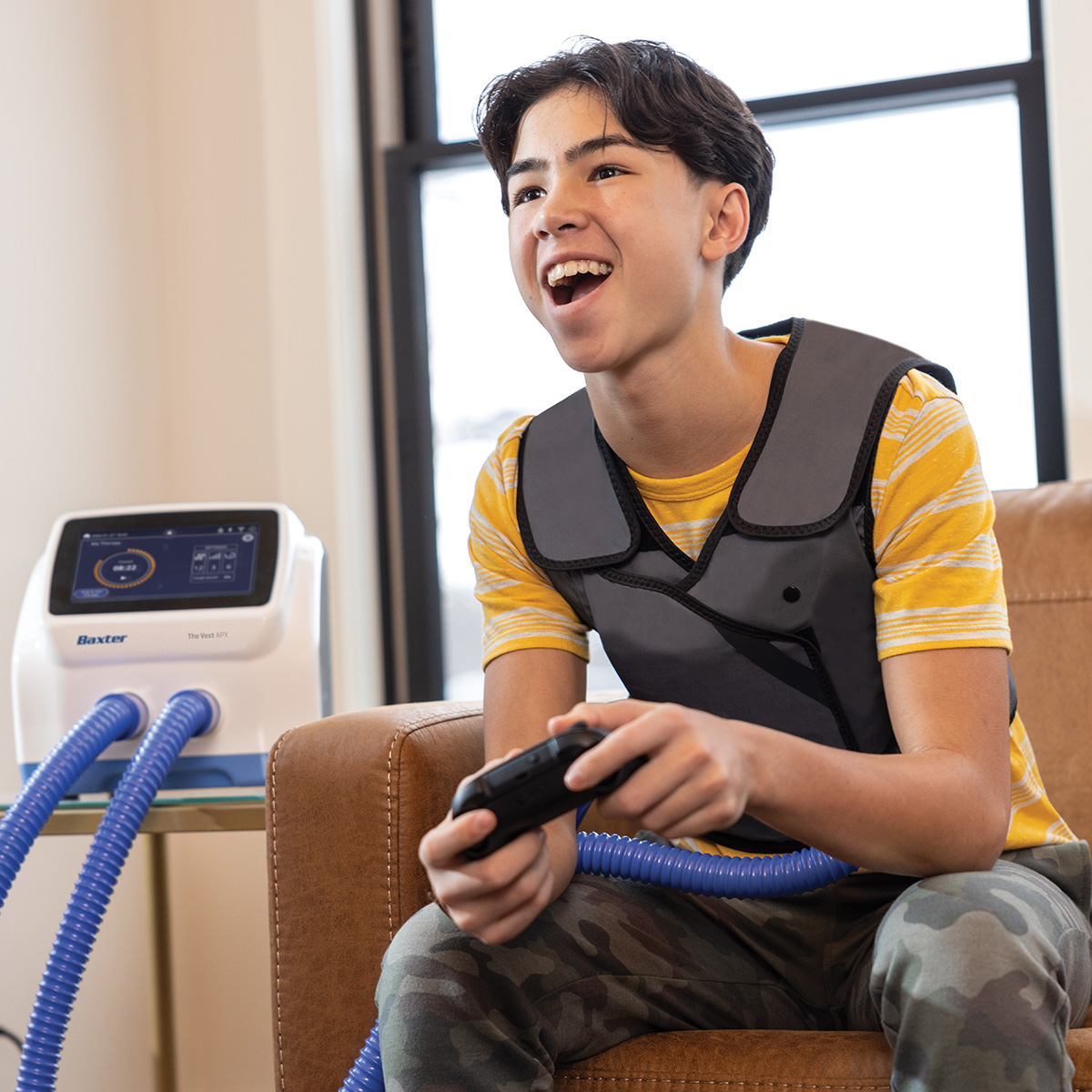 Image of a teenage boy wearing the vest garment for treatment while playing video games, with the control unit on a table next to him.