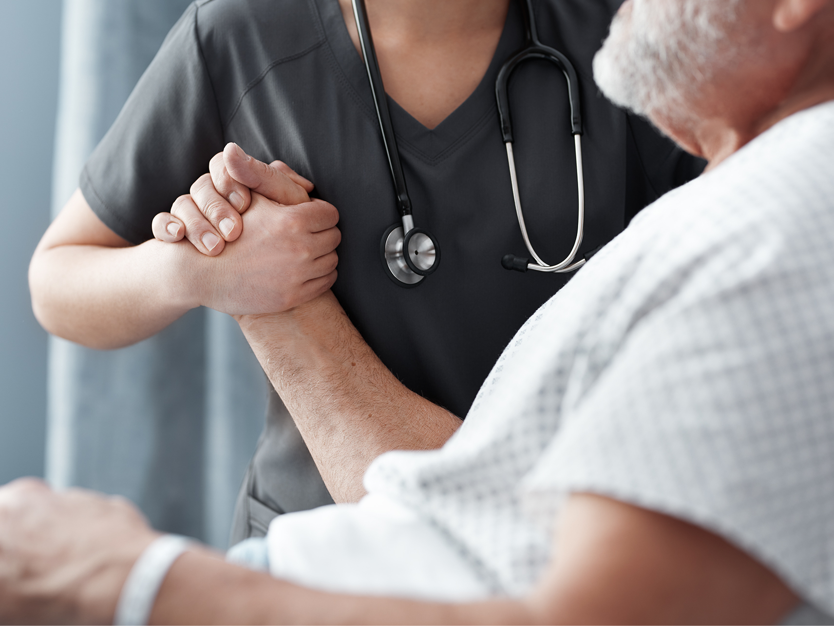 Caregiver assisting an elderly patient wearing a hospital gown